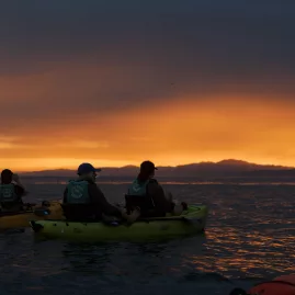 Kayakers float on still water under a dramatic, fiery sunset sky in Kaikōura
