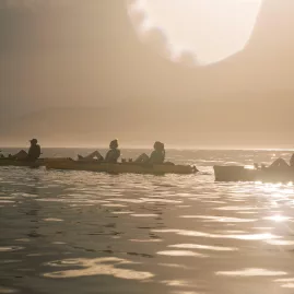 Silhouetted kayakers paddle across glassy waters with the Kaikōura Seaward Ranges behind