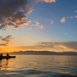 Two people kayaking on calm waters at sunset with the Kaikōura mountains in the distance
