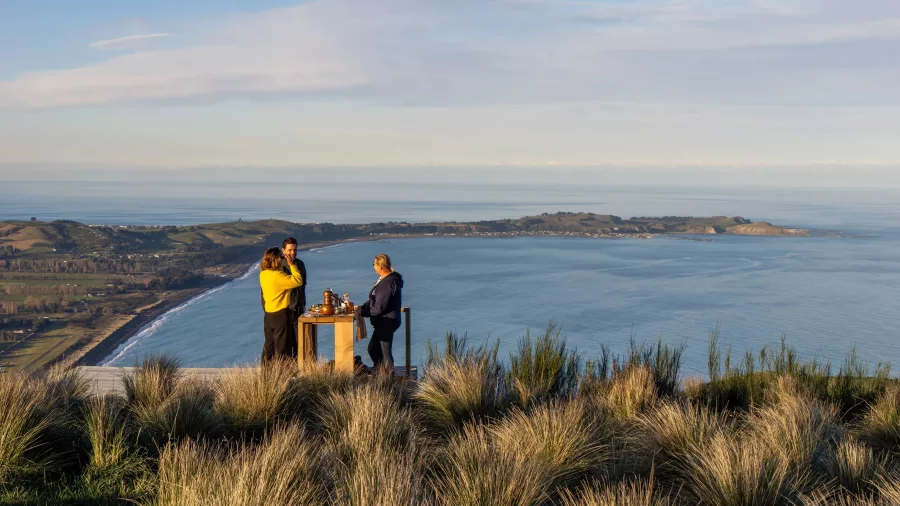 Two people enjoying gin tasting at scenic hilltop table overlooking Kaikōura coastline