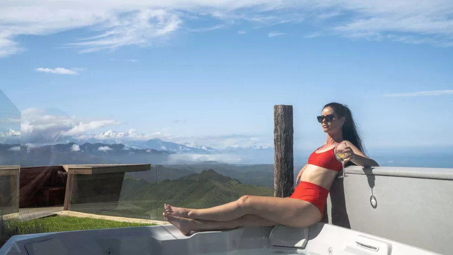 Woman in a spa pool with mountain and ocean views at Matai Peak retreat