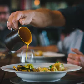 Chef pouring golden seasonal sauce over a plated dish at Hapuku Kitchen in Kaikōura