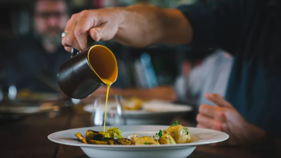 Chef pouring golden seasonal sauce over a plated dish at Hapuku Kitchen in Kaikōura