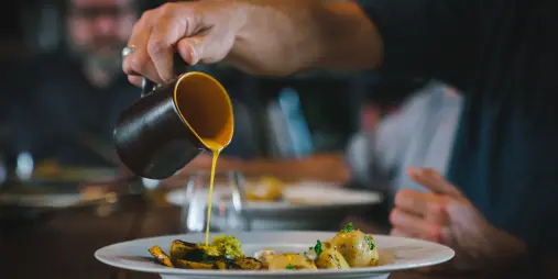 Chef pouring golden seasonal sauce over a plated dish at Hapuku Kitchen in Kaikōura