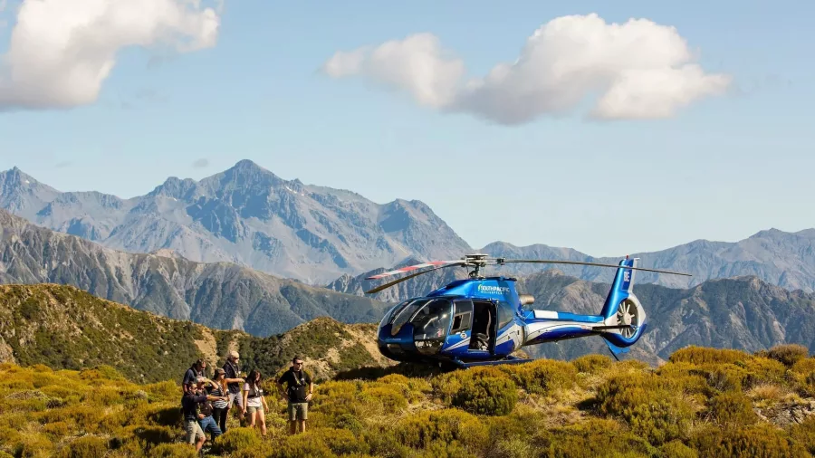 Group standing beside helicopter on scenic mountain landing during Kaikōura Ocean Safari