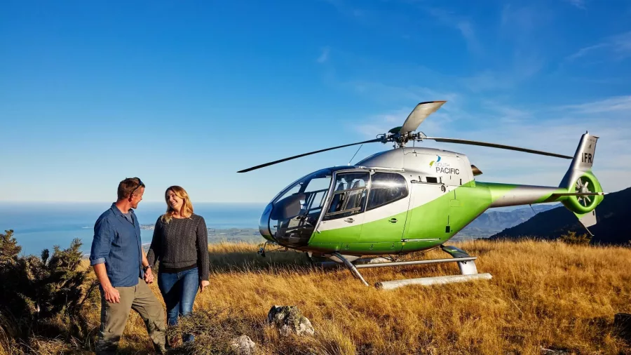 Couple enjoying private helicopter landing with Pacific Ocean views in Kaikōura
