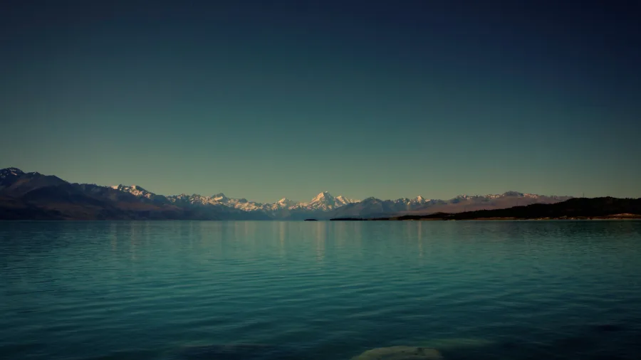 Lake Pukaki in New Zealand with turquoise waters reflecting the Southern Alps and Mount Cook (Aoraki) in the distance under a clear sky.
