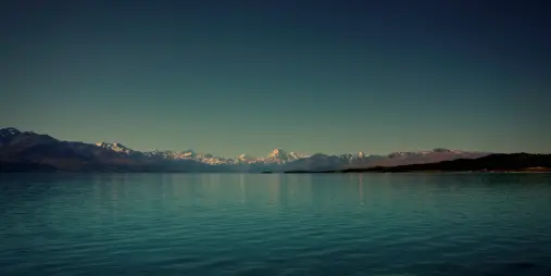 Lake Pukaki in New Zealand with turquoise waters reflecting the Southern Alps and Mount Cook (Aoraki) in the distance under a clear sky.