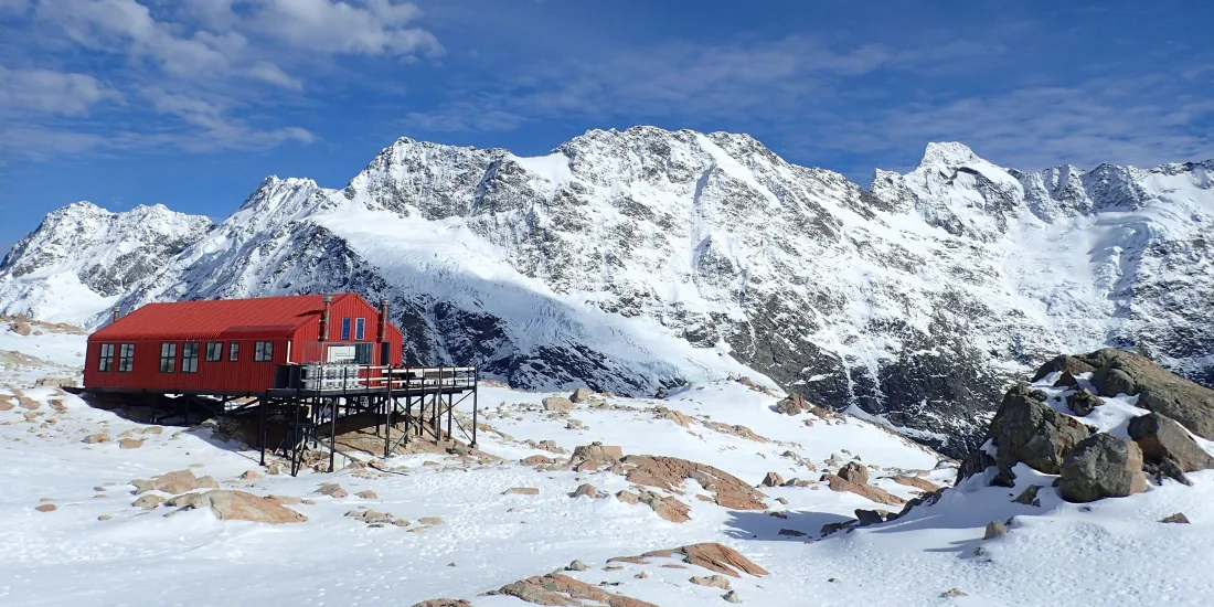 Wide view of Mueller Hut surrounded by snow and the Southern Alps under a crisp blue sky