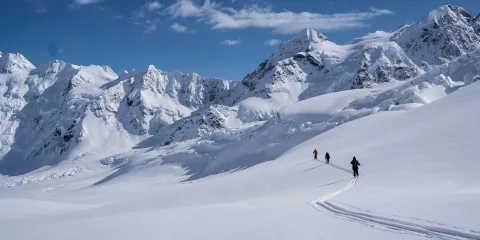Skiers heliskiing on the Tasman Glacier surrounded by the Southern Alps near Aoraki/Mount Cook, New Zealand.