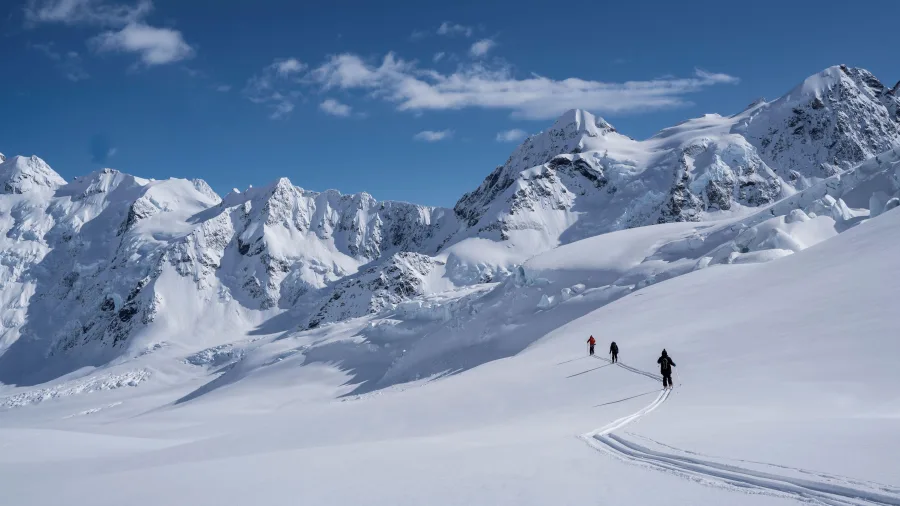 Skiers heliskiing on the Tasman Glacier surrounded by the Southern Alps near Aoraki/Mount Cook, New Zealand.