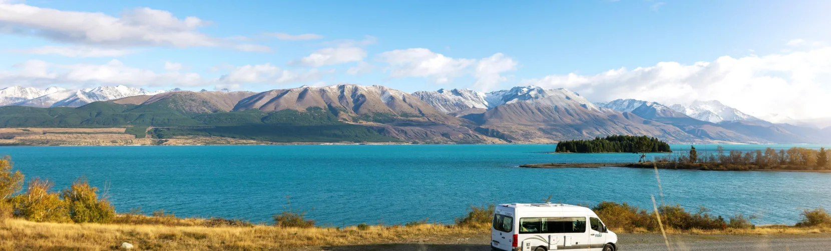 Campervan driving along Lake Pukaki with Southern Alps in the background
