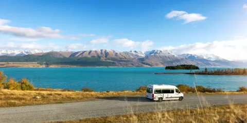 Campervan driving along Lake Pukaki with Southern Alps in the background