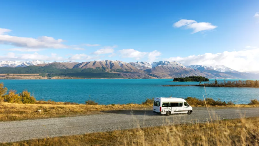 Campervan driving along Lake Pukaki with Southern Alps in the background