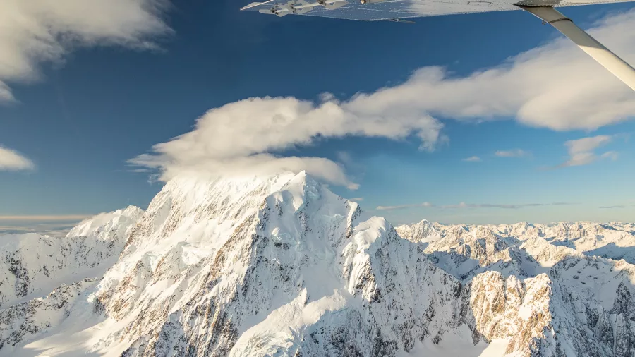 Aerial view of Mt Cook summit with lenticular cloud and wing of plane in foreground