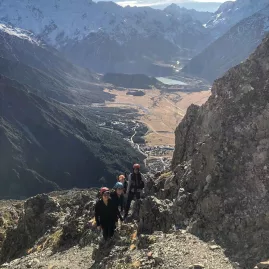 Group of hikers ascending the Mount Sebastopol trail with Aoraki/Mount Cook village visible far below.