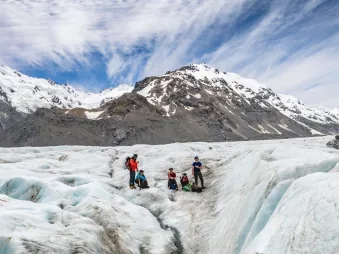 Small group exploring the ice on a private Tasman Glacier heli hike with mountains in the background.