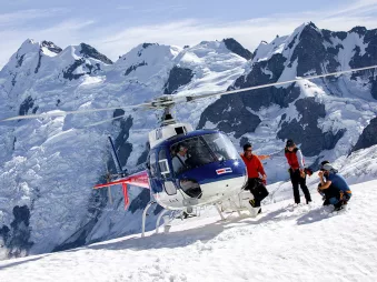 Private helicopter landed on a snowy slope above the Tasman Glacier with Aoraki/Mount Cook in the background.