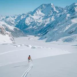 Solo skier descending a wide, powdery slope on Tasman Glacier with Aoraki/Mount Cook in the distance.