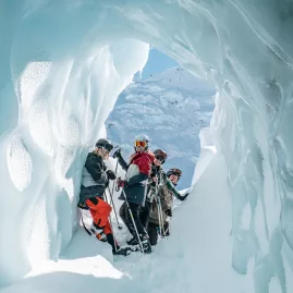 Group of skiers standing inside a sculpted glacier ice cave on the Tasman Glacier.