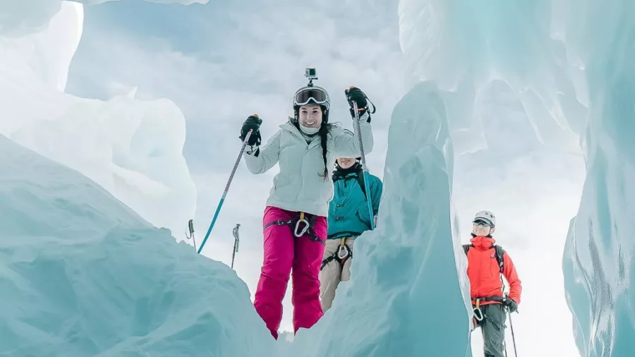 Skiers emerging from a beautiful ice cave on the Tasman Glacier with ski poles in hand.