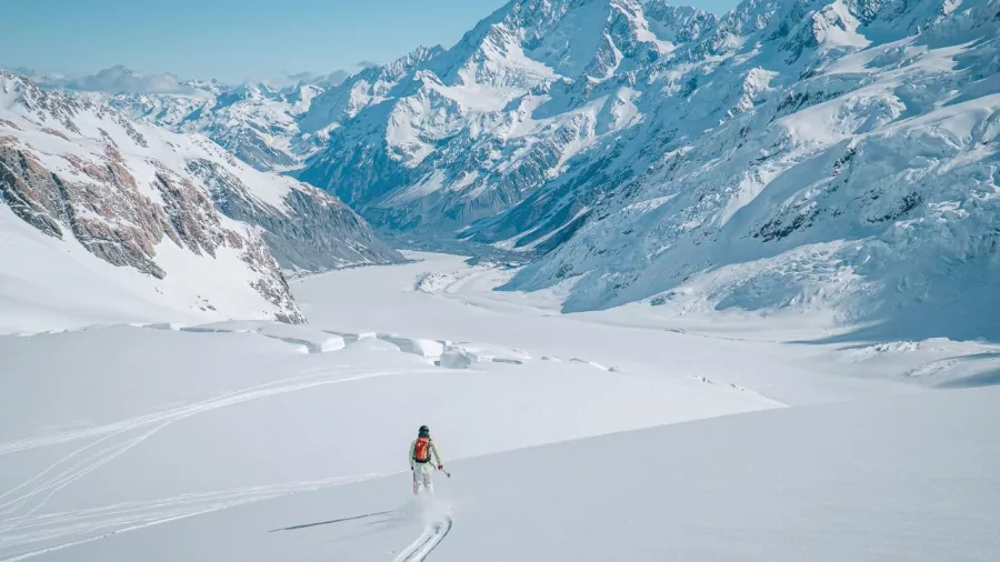 Solo skier descending a wide, powdery slope on Tasman Glacier with Aoraki/Mount Cook in the distance.