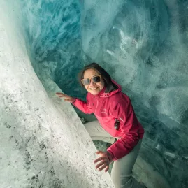 Smiling woman inside a glowing blue glacier tunnel on the Tasman Glacier.