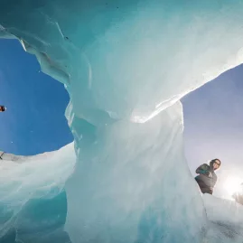 Group of hikers looking down through twin openings in glacier ice on Tasman Glacier.