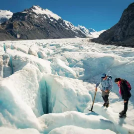 Guide showing a hiker around deep crevasses on Tasman Glacier with mountain views.