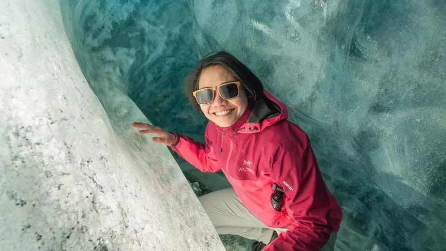 Smiling woman inside a glowing blue glacier tunnel on the Tasman Glacier.