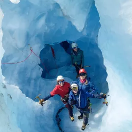 Group of ice climbers posing inside a striking blue ice cave on the Tasman Glacier.