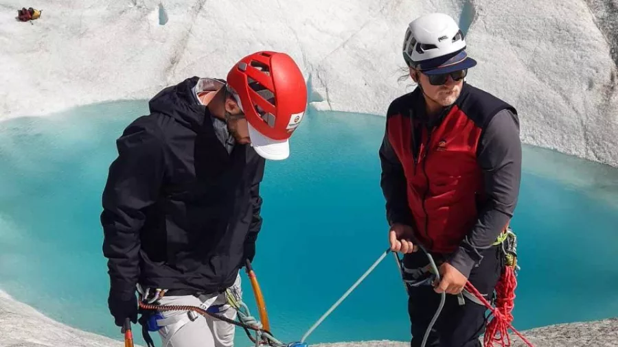 Two climbers setting up ropes beside a turquoise meltwater pool on the Tasman Glacier.