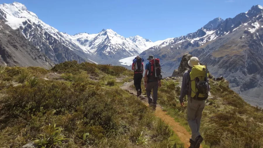 Group of hikers walking along a ridge with panoramic views of the Tasman Glacier below.