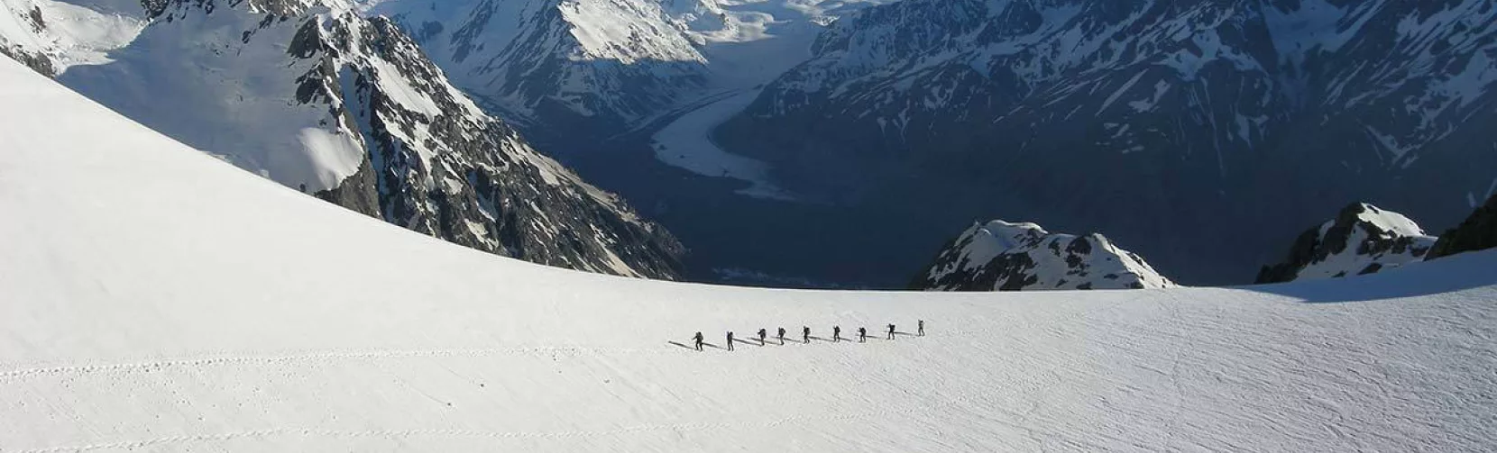 Group of trekkers walking across snowfields on Ball Glacier, overlooking Tasman Valley.