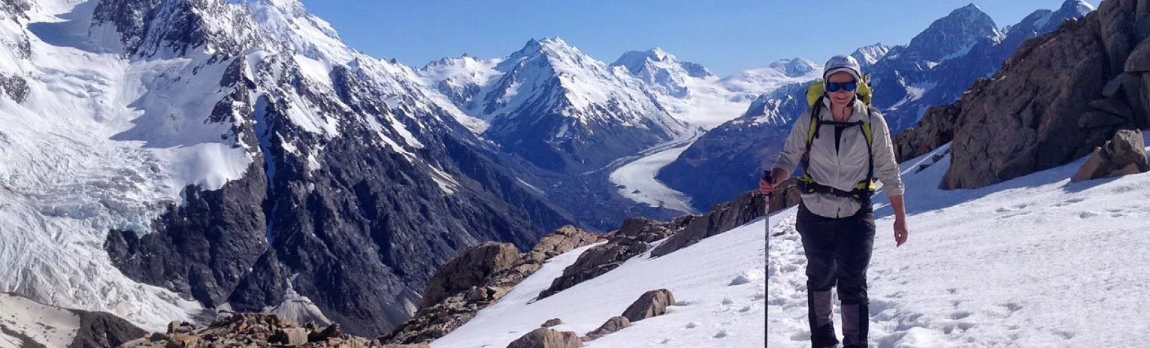 Solo hiker on snow-covered trail with panoramic views over the Tasman Glacier valley.