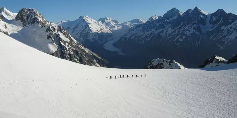 Group of trekkers walking across snowfields on Ball Glacier, overlooking Tasman Valley.