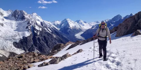 Solo hiker on snow-covered trail with panoramic views over the Tasman Glacier valley.