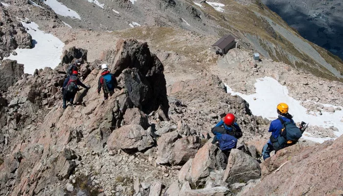 Group of trekkers scrambling over rocky terrain above Caroline Hut in Mount Cook National Park.