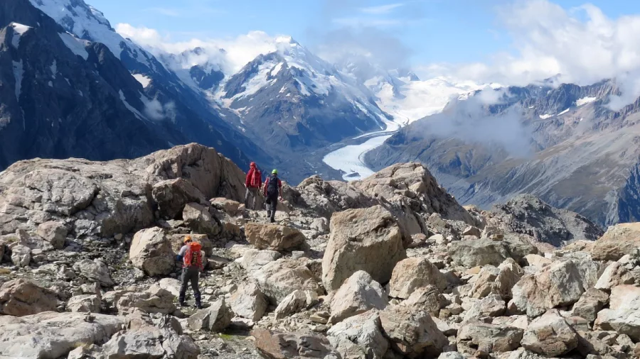 Hikers crossing the rocky terrain of Ball Pass with sweeping views of the Tasman Glacier in Aoraki Mount Cook National Park.