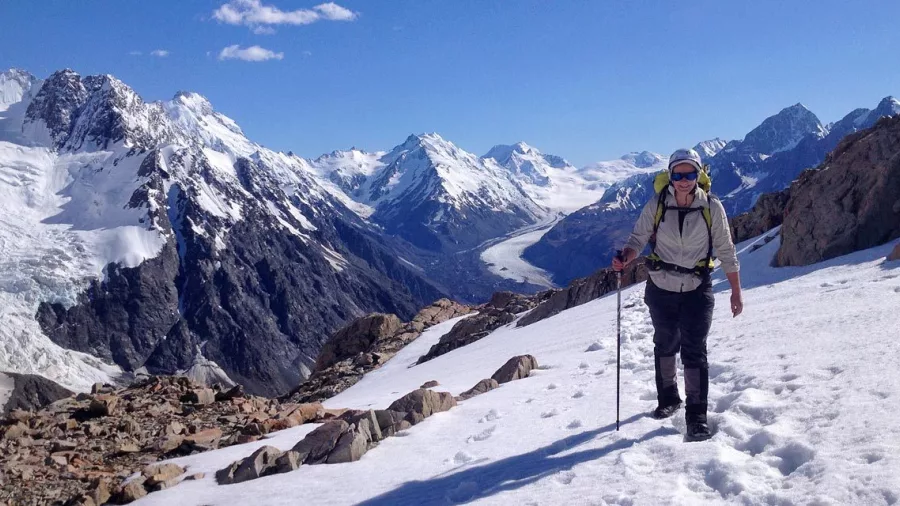 Solo hiker on snow-covered trail with panoramic views over the Tasman Glacier valley.