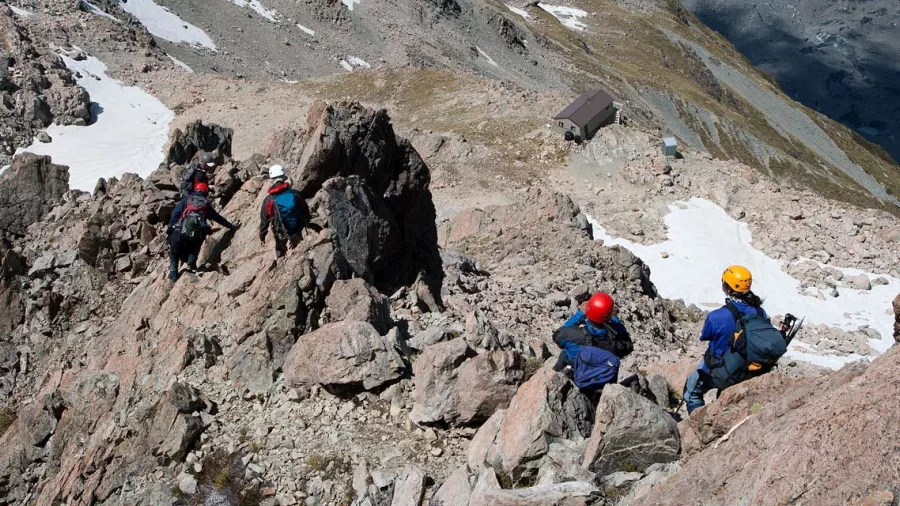 Group of trekkers scrambling over rocky terrain above Caroline Hut in Mount Cook National Park.