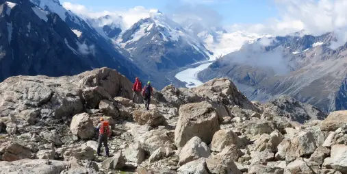 Hikers crossing the rocky terrain of Ball Pass with sweeping views of the Tasman Glacier in Aoraki Mount Cook National Park.