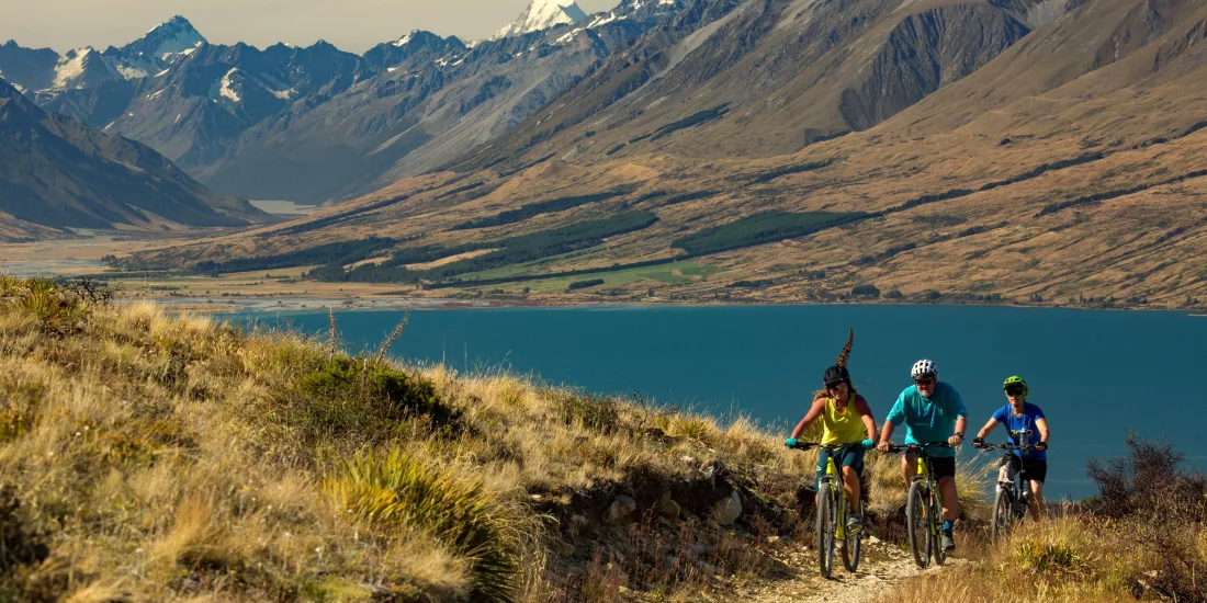 Cyclists riding the Alps 2 Ocean Cycle Trail near Sailor’s Cutting with Lake Benmore and mountain views