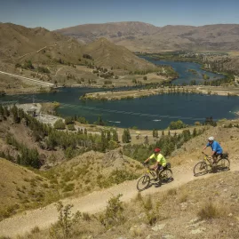 Two cyclists riding above the Aviemore Dam near Otematata with sweeping river views on the Alps 2 Ocean Trail