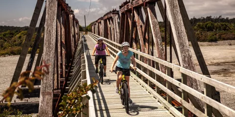 Cyclists crossing the Totara River Rail Bridge, a historic Howe Truss structure on the West Coast Wilderness Trail