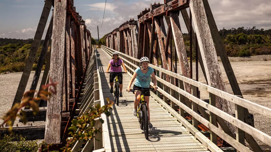 Cyclists crossing the Totara River Rail Bridge, a historic Howe Truss structure on the West Coast Wilderness Trail