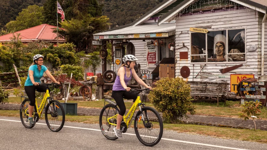 Cyclists riding past a historic building in Ross on the West Coast Wilderness Trail