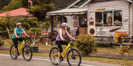 Cyclists riding past a historic building in Ross on the West Coast Wilderness Trail
