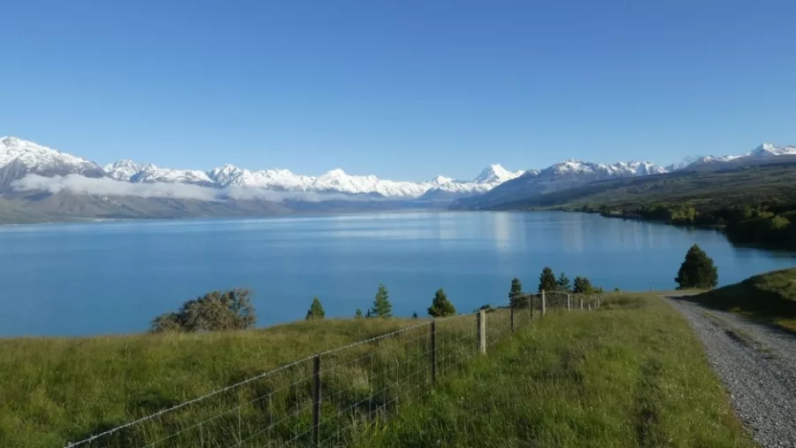 Gravel cycle trail beside Lake Ohau with panoramic views of snow-covered Southern Alps in the distance