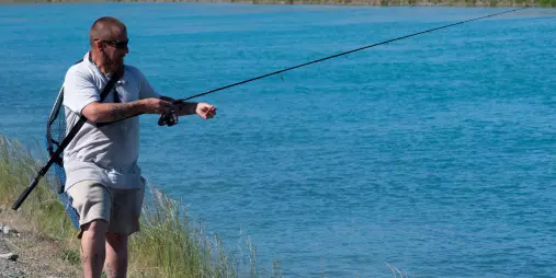 Fisherman casting line into the clear waters of Lake Tekapo canal during a guided fishing experience
